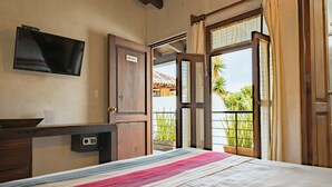 A hotel room with a bed, a desk with a flat-screen TV, a wooden door, and a balcony with plants. - Yox Hotel Boutique (San Cristóbal de las Casas)