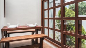 A wooden dining table with white plates and cups, set against a white wall with a large window overlooking greenery. - Yox Hotel Boutique (San Cristóbal de las Casas)