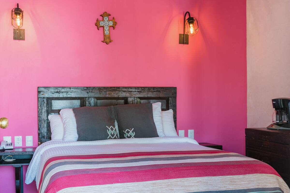 A bedroom with a pink wall, a wooden headboard, a striped bedspread, and two wall-mounted light fixtures.