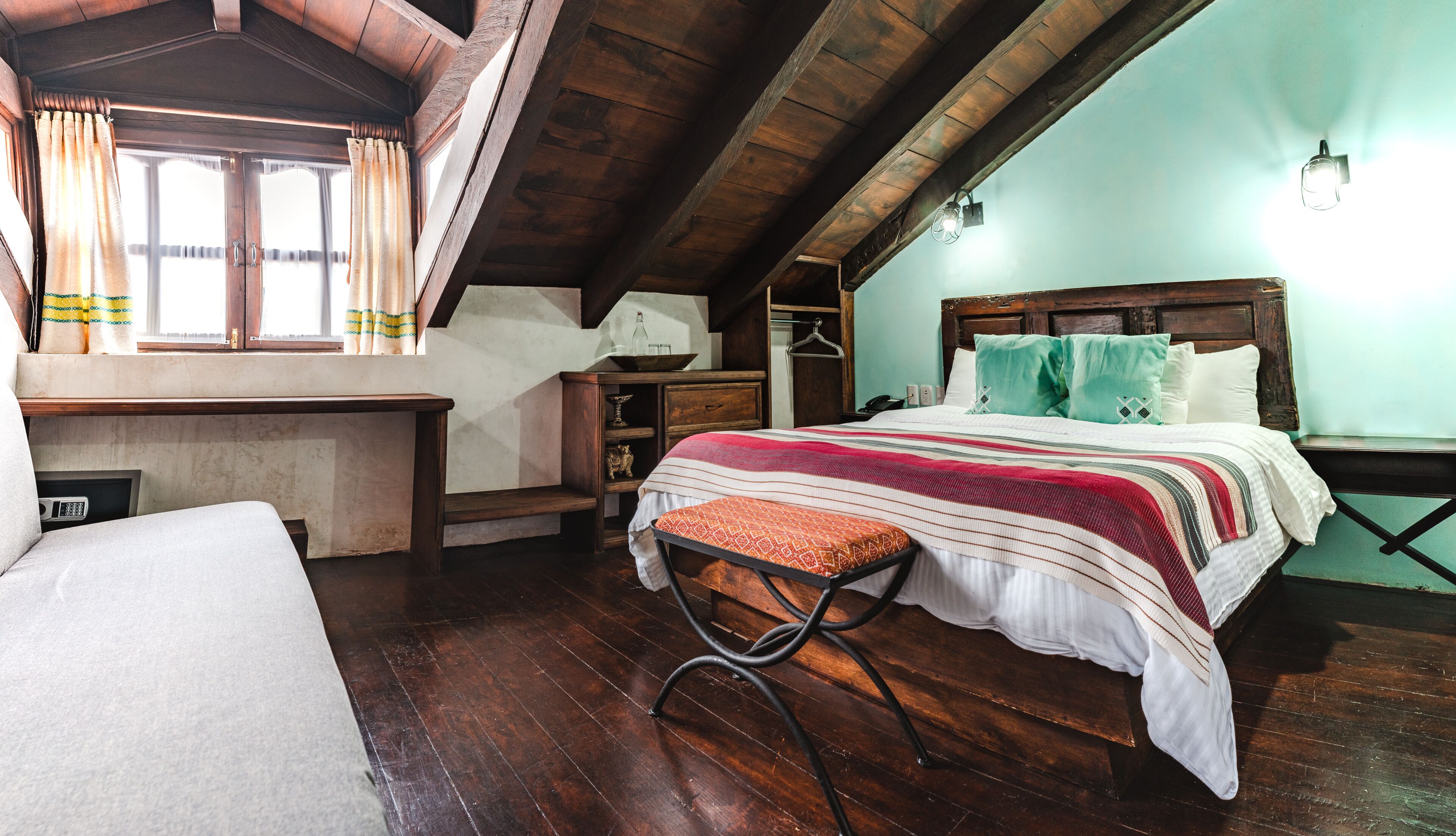 A cozy attic bedroom with a wooden bed, a desk, and a window with curtains.