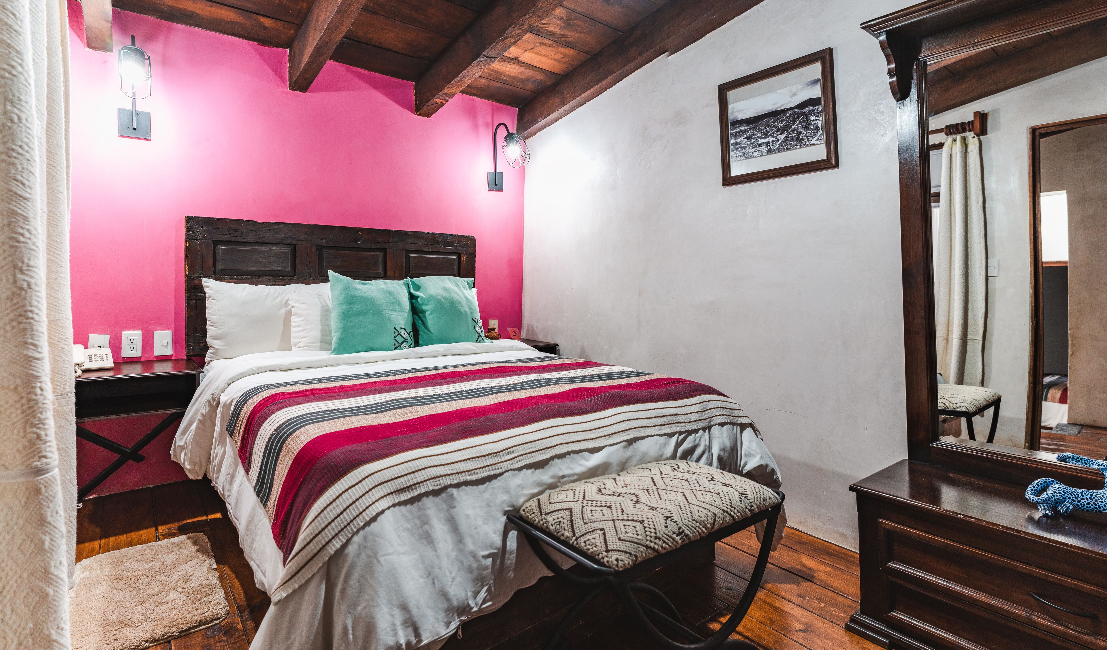 Un dormitorio con cabecera de madera, una cama con manta a rayas, una mesita de noche con un teléfono y un espejo con una toalla de estampado de leopardo.