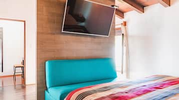 A bedroom with a teal bed, a colorful blanket, a mounted TV, and a wooden ceiling.