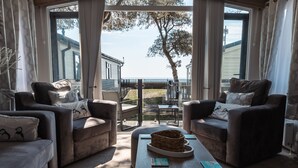 A living room with two sofas, a coffee table, and a view of the sea. - The Harris Hut - a fantastic new property on Sandhills Holiday Park, Mudeford (Christchurch)