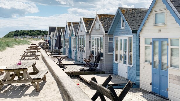 A row of beach huts with wooden benches and tables, a sandy beach, and a clear sky. - The Harris Hut - a fantastic new property on Sandhills Holiday Park, Mudeford (Christchurch)