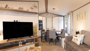 A modern living room with a flat-screen TV, a wooden coffee table, and a sofa with decorative pillows. - The Harris Hut - a fantastic new property on Sandhills Holiday Park, Mudeford (Christchurch)