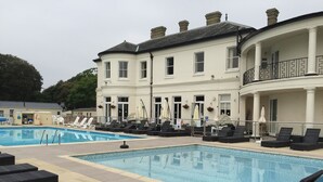 A pool area with lounge chairs and a building with multiple windows and a balcony.