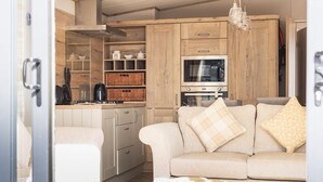 A compact kitchen with wooden cabinets, a built-in oven, and a microwave. There is a beige sofa with patterned cushions in the living area.