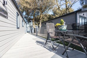 A covered outdoor area with a metal table and chairs, a potted plant, and a sign on the building.