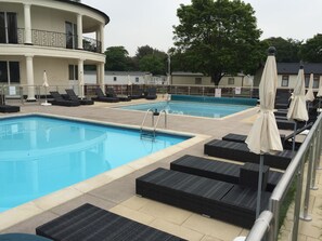 A pool area with lounge chairs and umbrellas, a pool, and a building with a balcony.