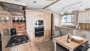 A modern kitchen with wooden cabinets, a gas stove, an oven, and a dining area with a table and chairs.