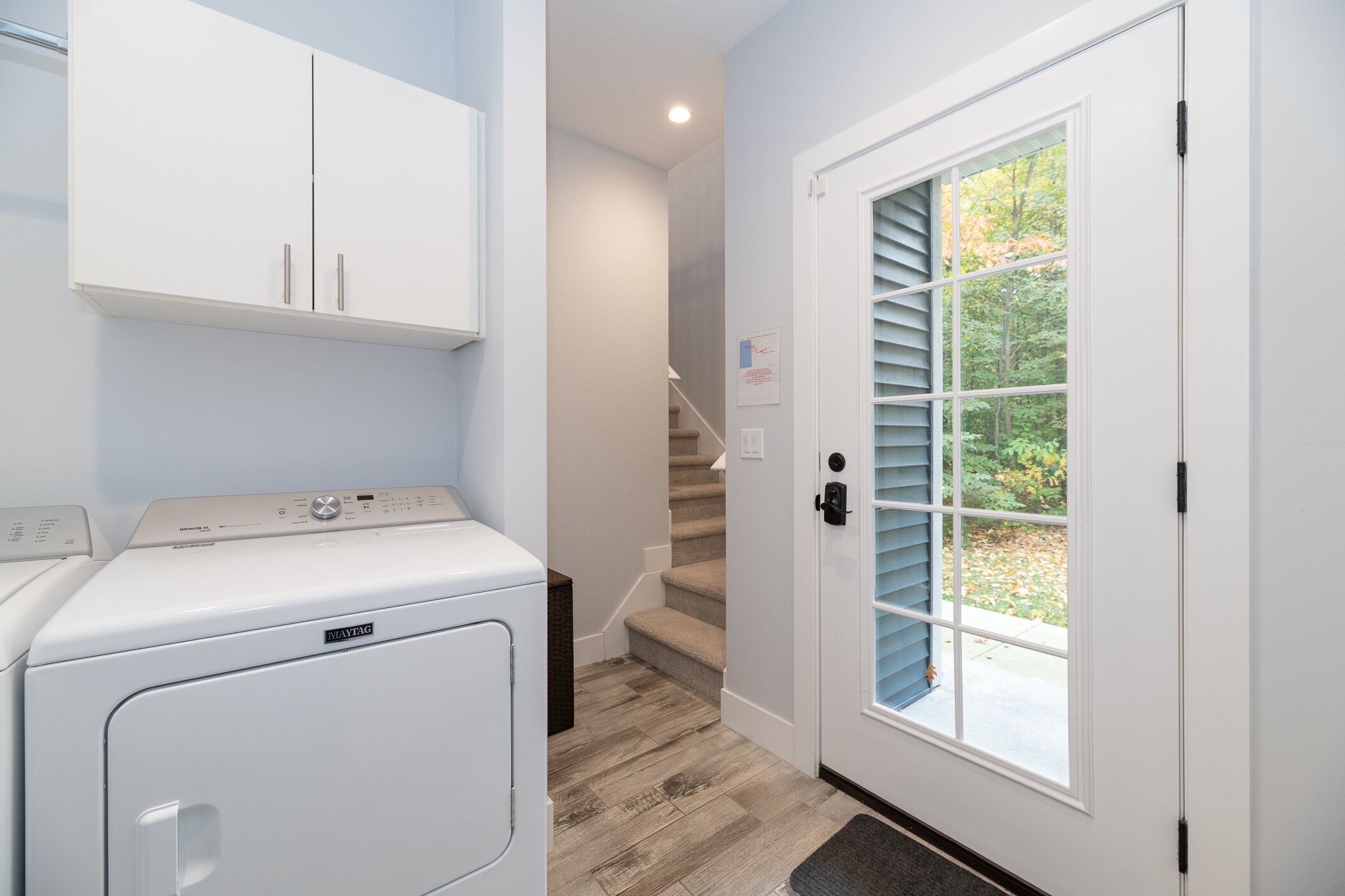 A laundry room with a front-loading washer and dryer, a staircase leading to another level, and a door with a view of the outdoors.