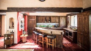 A rustic kitchen with wooden cabinets, a central island with stools, and a decorative backsplash.