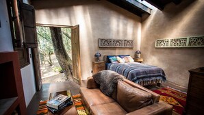 A cozy room with a bed, a leather sofa, a wooden nightstand, and a window with a view of trees.