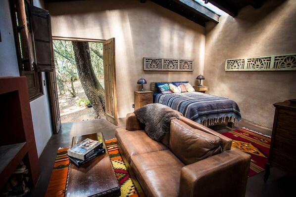 A cozy room with a bed, a leather sofa, a wooden nightstand, and a window with a view of trees.