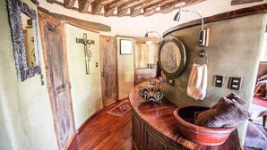 A rustic bathroom with wooden floors, a wooden vanity, a mirror, a towel rack, and a wooden cross on the wall.