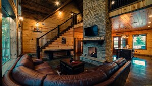 A spacious living room with a stone fireplace, leather sofa, and a staircase leading to an upper level. - Fishin' in the Dark- private shoreline view for lounging or fishing (broken bow)