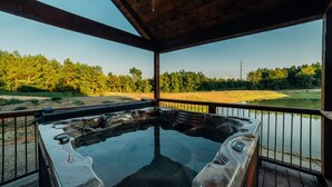 A hot tub with a wooden deck and railing, overlooking a lake and forested area. - Fishin' in the Dark- private shoreline view for lounging or fishing (broken bow)