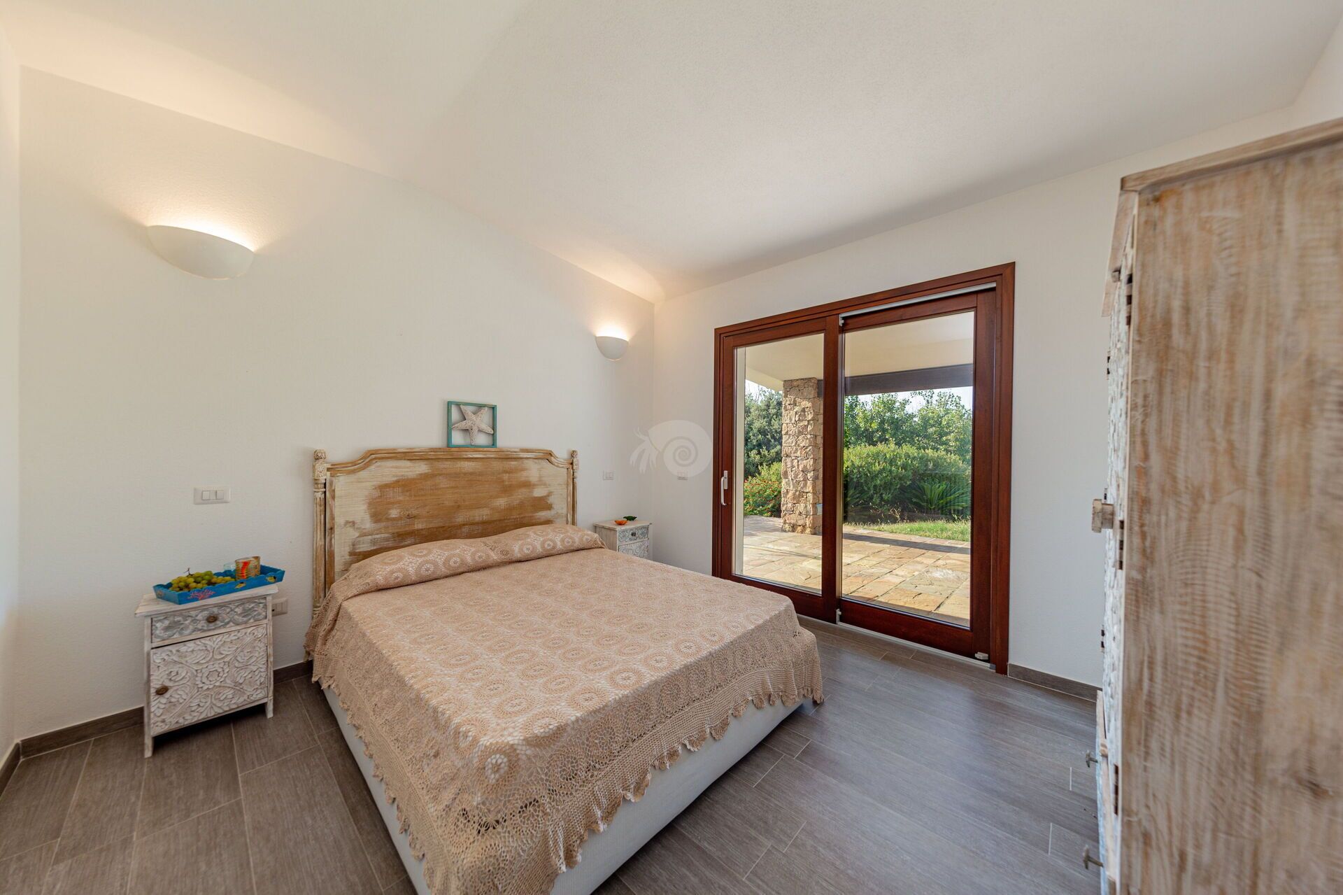 Une chambre à coucher comprenant un lit, une table de chevet, une commode, une décoration en forme d’étoile de mer et une porte-fenêtre coulissante donnant sur un espace extérieur.