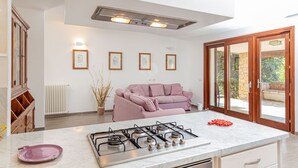 A modern kitchen with a gas stove, a pink sofa, and framed pictures on the wall. - Villa Belle: private pool near the beach (Aglientu)