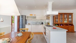 A modern kitchen with white cabinetry, a central island, a built-in oven, and a wooden cabinet with glass doors. - Villa Belle: private pool near the beach (Aglientu)