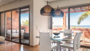 A modern dining area with a glass table and white chairs, large sliding glass doors leading to a balcony with a view of the beach. - Bahia - Alzaro 1.2 DELUXE SEA VIEW & JACUZZI 3B (Arona)
