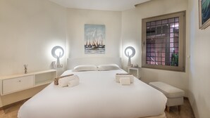 A bedroom with a large bed, two bedside tables with lamps, a window with a grid pattern, and a painting of sailboats on the wall. - Bahia - Alzaro 1.2 DELUXE SEA VIEW & JACUZZI 3B (Arona)