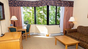 Een hotelkamer met een eettafel, twee stoelen, een bank en een raam met gordijnen.
