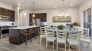 A modern kitchen with a central island, stainless steel appliances, and a dining area with white chairs.