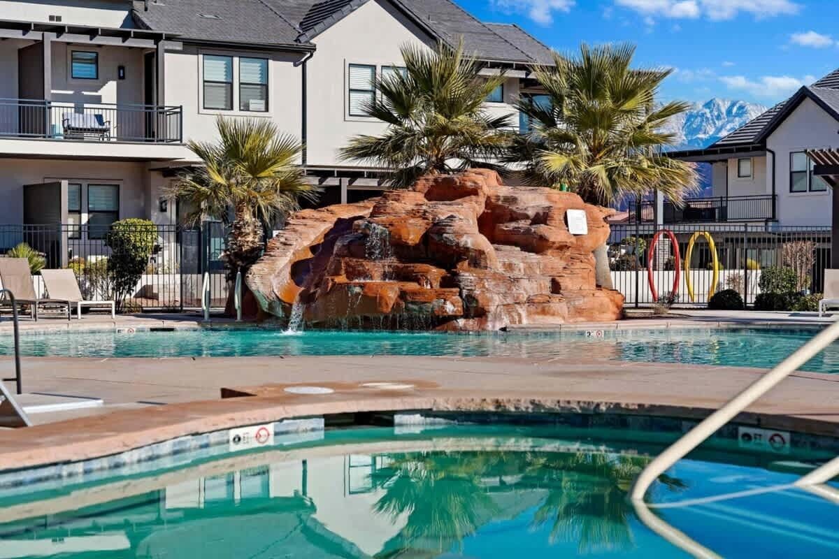 Une piscine agrémentée d’une cascade artificielle en roches, entourée de palmiers et bordée d’un immeuble d’habitation.
