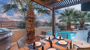 An outdoor patio with a pool, a grill, and dining tables set for a meal.