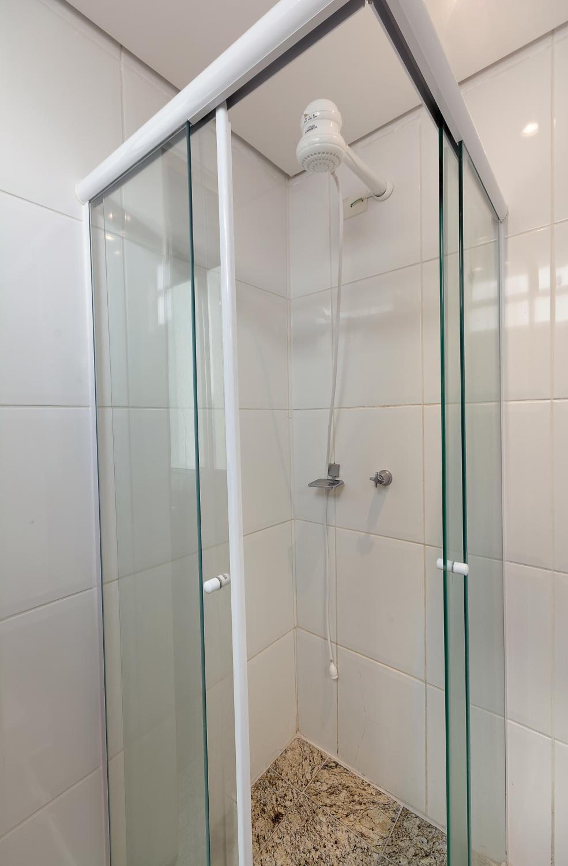 Cabina doccia con pareti in vetro, soffione a mano e manopola di regolazione.
