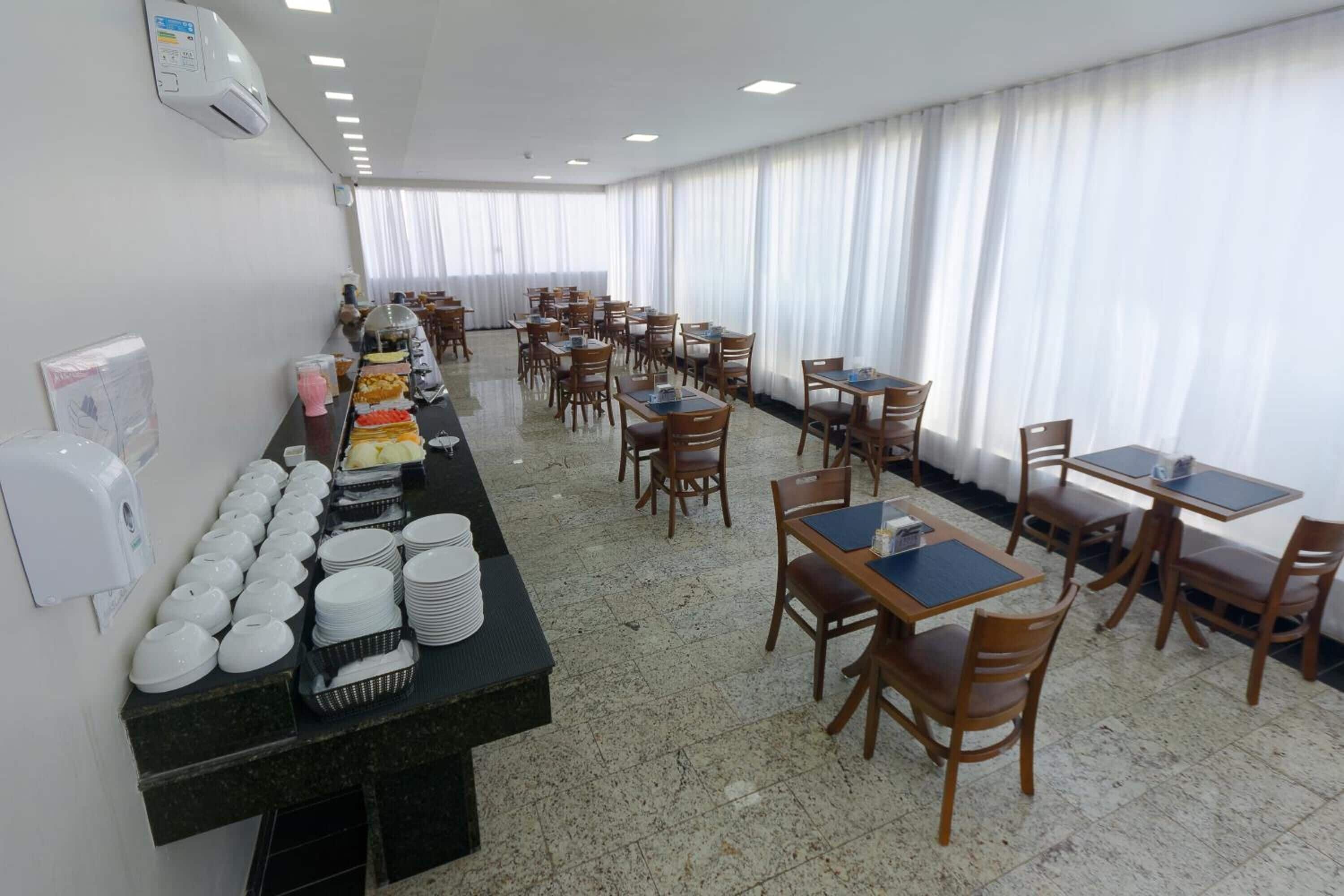 A dining area with tables and chairs, a buffet counter with plates and bowls, and a window with curtains.