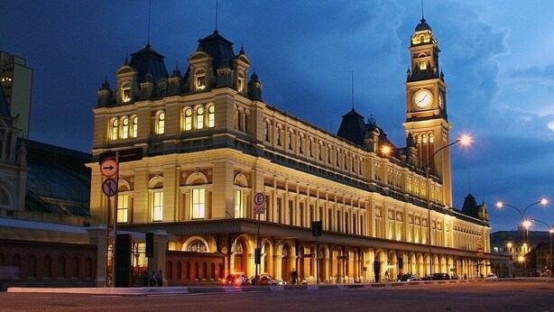 Un edificio histórico con una imponente torre del reloj, grandes ventanales de arco y una fachada simétrica.