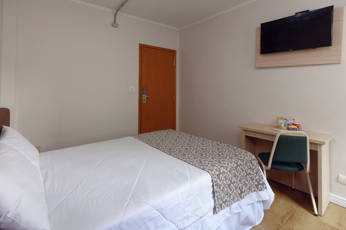 A bedroom with a bed, a desk, a chair, a television, and a door.