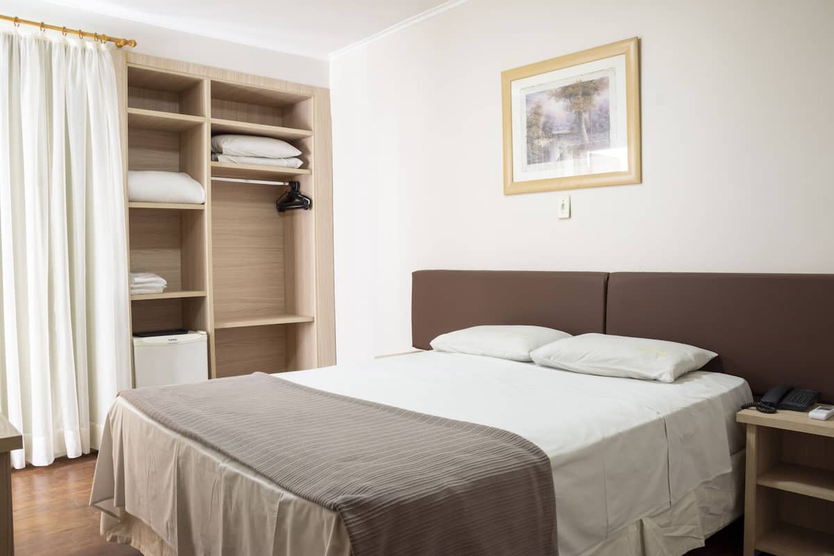 A neatly arranged bedroom with a bed, a bedside table, a wardrobe, and a framed picture on the wall.