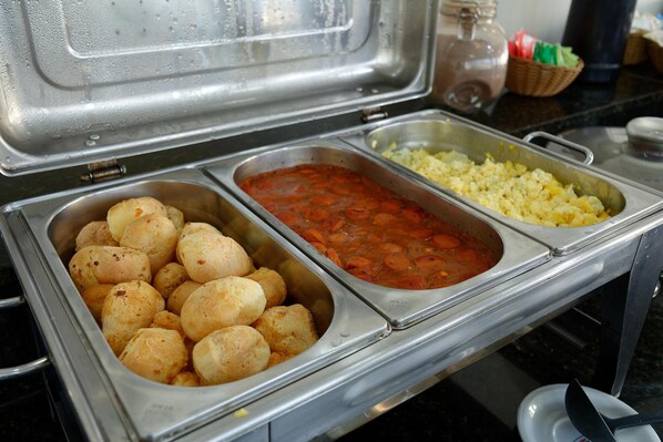 A buffet with three food stations: one with bread rolls, one with a red sauce, and one with rice.