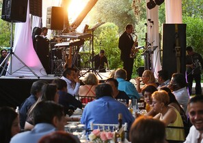Une scène où des musiciens se produisent, entourés d’invités assis.