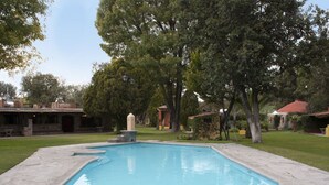 A rectangular swimming pool with a stone border, surrounded by a grassy area and trees. - Cabañas Quinta Patricia (Tequisquiapan)