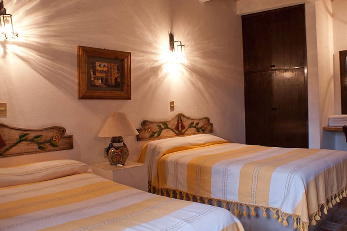 A hotel room with two beds, a wooden headboard, a nightstand with a lamp, and a framed picture on the wall.