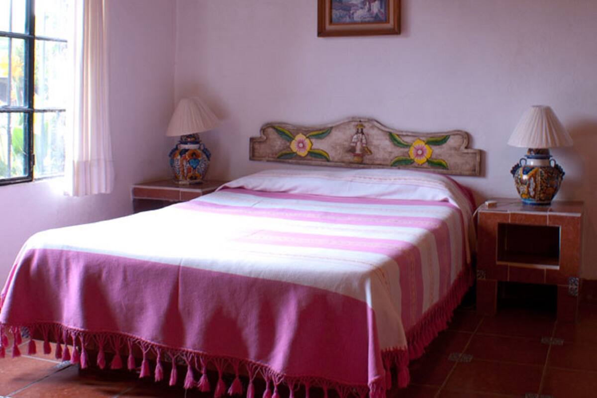 A neatly made bed with a pink and white striped bedspread, two bedside tables with lamps, and a framed picture on the wall.