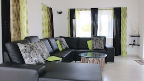 Uma sala de estar moderna com um sofá modular preto, uma mesa de centro de vidro e uma grande janela com cortinas.