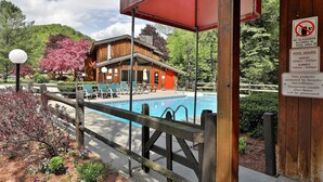 Una cabaña de madera con piscina, rodeada por un seto de madera y árboles de cerezo.