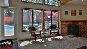 Una habitación con ventanas amplias, chimenea y mobiliario exterior junto a la piscina.