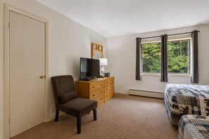 A bedroom with a bed, a chair, a dresser, a television, and a window with curtains.