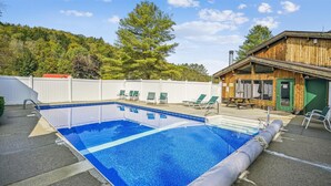 Une piscine extérieure rectangulaire à l’eau d’un bleu limpide, entourée d’une clôture blanche, et un bâtiment en bois avec une porte verte sur le côté droit.