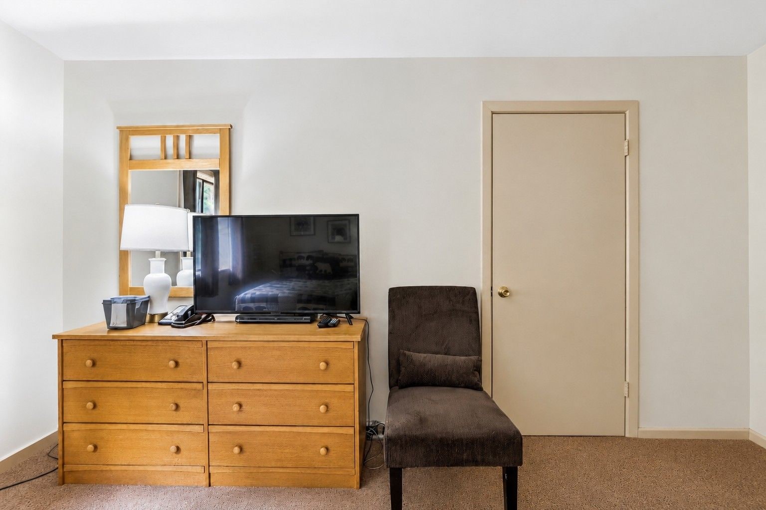 A hotel room with a wooden dresser, a television, a chair, and a door.