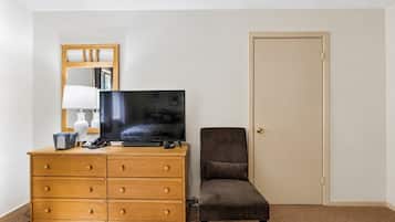 A hotel room with a wooden dresser, a television, a chair, and a door.