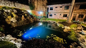 A serene indoor garden with a pond, a Buddha statue, and a stone building with multiple windows. - Hotel Villa Pralaya (Jiutepec)