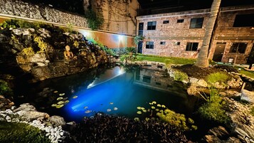 Un jardín interior tranquilo con un estanque, una estatua de Buda y un edificio de piedra con varias ventanas.