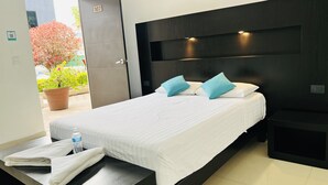 A modern hotel room with a large bed, a nightstand, and a view of a garden. - Hotel Villa Pralaya (Jiutepec)